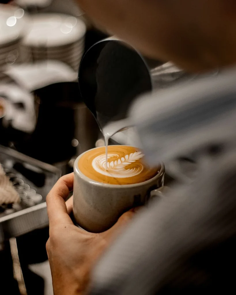 Hands crafting a flat white coffee with latte art in a cozy New Zealand café.