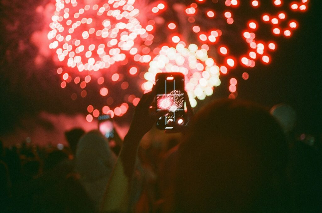 a photo from behind a woman of her taking a picture of fireworks with her phone.