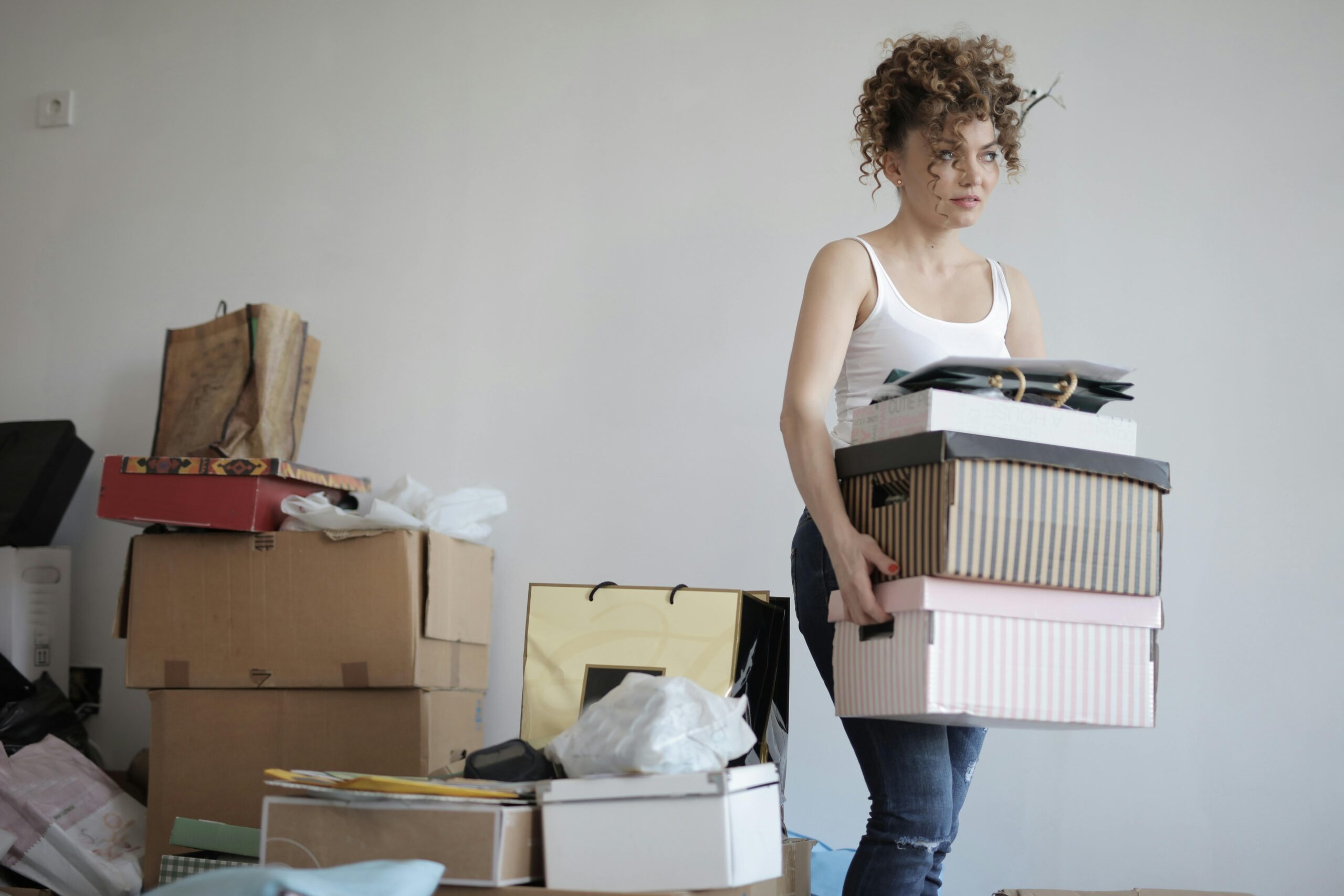 Tired, sad woman packing for a long journey, she is carrying many overfilled boxes and bags